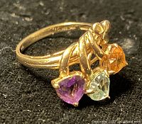 Oblique view of ring showing three heart-shaped gemstones in purple, light green, and orange