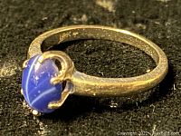 Front view of ring showing oval blue cabochon stone with white banding in prong setting