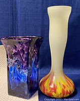 Pair of two multicoloured blown glass vases on a neutral surface with a blue fabric background.