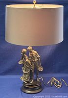 Front view of lamp with shade attached, showing figural base and cord coiled beside it.