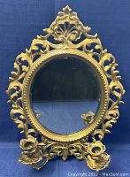 Front view of oval brass boudoir mirror with ornate detailing and two candle holders at base.