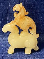 Front and side view of the small carved jade mythical creature sculpture on dark fabric background