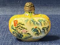 Front view of oval enamel snuff bottle with detailed hand painted landscape on yellow background.