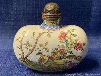 Front side of white enamel snuff bottle with hand painted floral and bird design, metal decorated cap visible at top.