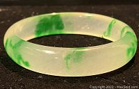 Side view of translucent pale green jade bangle with dark green marbling on a black background