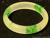 Close-up photo of the jade bangle showing translucent light green color with multiple green spots and marbling.