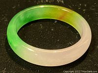 Close-up angled photo showing the smooth glossy finish and bicolor tones of white and green jade with a small brown tint.