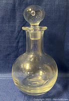 Full view of the clear glass decanter with stopper in place, showing the round body and flared neck.