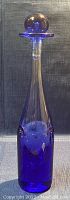 Full view of the cobalt blue blown glass decanter with stopper in place, showing slender shape and curved profile.