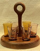 Photo of the teak wood caddy holding six shot glasses, four purple tinted glass and two amber plastic, arranged around the handle.