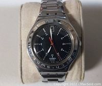 Front view showing the black dial, silver hands, red second hand, and date display at 12 o'clock. Stainless steel bezel engraved with 'swatch'.