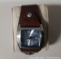 Front view of the Fossil watch showing the square silver case, gray dial with date window, and brown leather strap with metal studs.