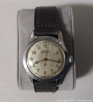 Front view of watch on display cushion showing stainless steel case, silver dial marked GRUEN Veri-Thin and leather strap.