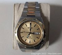 Front view of Seiko watch showing gold-tone dial with day/date display and two-tone metal bracelet.