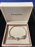 Pandora silver charm bracelet displayed inside original Pandora box with soft cream and pink lining.