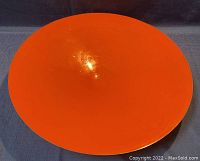 Top view of large round orange enamel wall art showing smooth glossy surface with minor blemishes and chips.