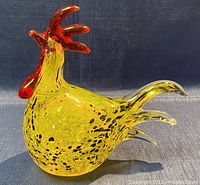 Front and left side profile of yellow and black speckled blown glass rooster with red comb and wattles. One eye is missing.