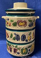 Front view of vintage rumtopf canister showing embossed and colorful fruit designs on cream and green bands.