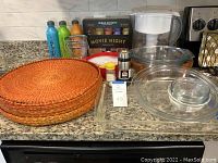 Overview of glass bakeware including rectangular dish, round plates, bowl, water pitcher, woven placemats, popcorn set, and seasoning containers on granite countertop.