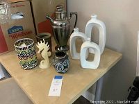 Overview photo showing all items including white sculpture vases, silver plated server, pottery vases, candle holder, and seahorse sculpture.