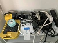 Photo showing yellow surge protector, light blue alarm clock, black flashlight, white Midland weather radio, and black and white cords.
