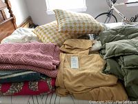 Full view of linens on bed, showing pillows, knitted pink throw, floral blanket, tan mattress pad, and green quilt.