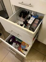 Open drawer showing multiple bottles of nail polish and makeup products organized in white plastic containers, plus boxed hair dryers below.