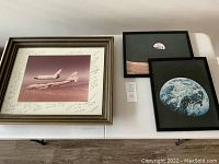 Wide view of all three framed photographs on a white table. The space shuttle photo is on the left, moon photos on the right.