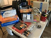 Overview of table with batteries, boxes of paper, envelopes, mesh organizers, pens and scissors in containers
