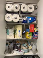 Full linen closet shelf showing paper towels on top, paper towels and kitchen wraps in middle, disposable plates and utensils on bottom.