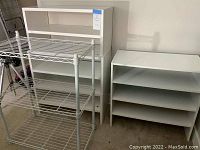 Photo showing four white stackable rectangular wooden shoe shelves side by side along wall and white wire shoe shelf in foreground