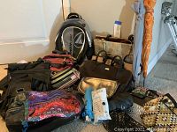 Photo of all bags, backpacks, umbrellas on floor along wall showing range of items.