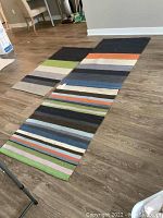 Two wool flat weave rugs laid out on a wood floor showing rectangular rugs with horizontal color block and stripe patterns.