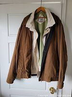 Men's brown jacket with beige inner lining and elastic cuffs hanging on wooden hanger