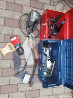 Overview of open red and blue toolboxes showing long hand tools and small items laid out on brick surface