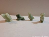 Front view of 4 pale green jade animal figurines including elephant, horse, bird, and owl.