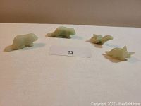 Photo showing all four light green jade animal figurines arranged in a line on a flat surface with a lot number card in front.