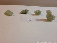 Four light green jade animal figurines displayed in a row on a white surface with a lot number card '36'.
