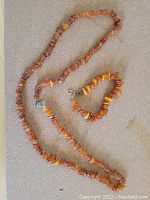 Photo of amber chip necklace and bracelet laid flat on a neutral surface showing overall color and clasp details.