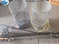 Two cylindrical wire mesh bait fish traps and three old fishing rods with reels and handles visible, placed on concrete floor.