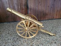Side angle showing polished brass cannon with detailed spoked wheels and tapered barrel.