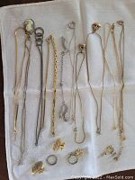 Photo showing various gold-tone and silver-tone costume jewellery items including nine necklaces and bracelets, three pairs of clip-on earrings, and two rings laid out on a white cloth.