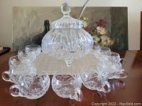 Crystal punch bowl set arranged on table showing bowl with lid, ladle, and 12 matching cups with etched floral and starburst designs.