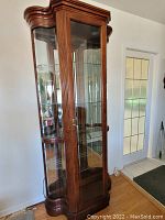 Full view of the curio cabinet showing its tall narrow shape, dark wood finish, glass door and sides, and overall condition.