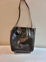 Full front view of the brown Danier leather handbag with front flap pocket and two short handles, one long shoulder strap.