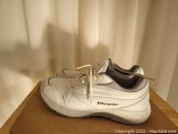 Side view of white Etonic running shoe on a cardboard surface, showing the Etonic logo and shoe design details.