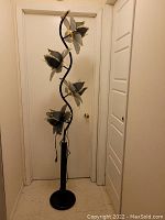 Front view of entire lamp showing twisted black metal stem and three stacked flower-shaped metal shades
