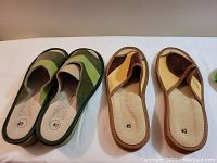 Top view of two pairs of leather slippers, one in green shades and one in tan and brown, showing size 40 markings.