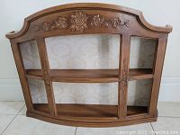 Front view of mini wooden wall display cabinet with glass front and floral carved decor along the top edge.