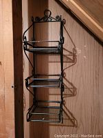 Photo of a black metal mini wall rack with three mesh shelves mounted on a wooden wall.